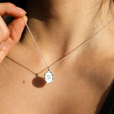 Person wearing a silver necklace with a pendant engraved with cursive letters