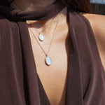 Close-up of a person wearing a brown garment with a necklace featuring two oval silver pendants.