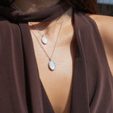 Close-up of a person wearing a brown garment with a necklace featuring two oval silver pendants.