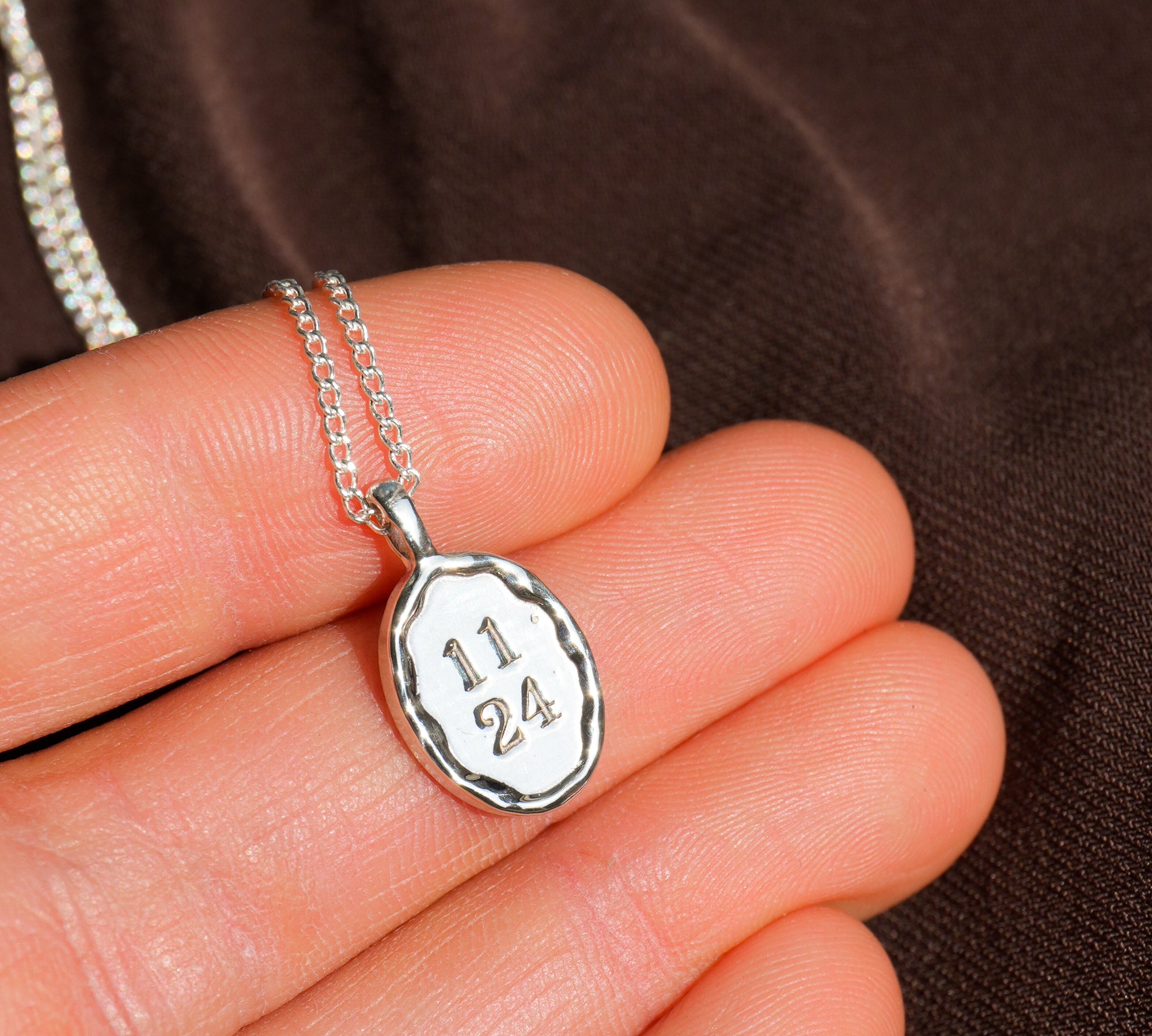 Silver necklace with a pendant engraved with numbers held in a hand against a brown background