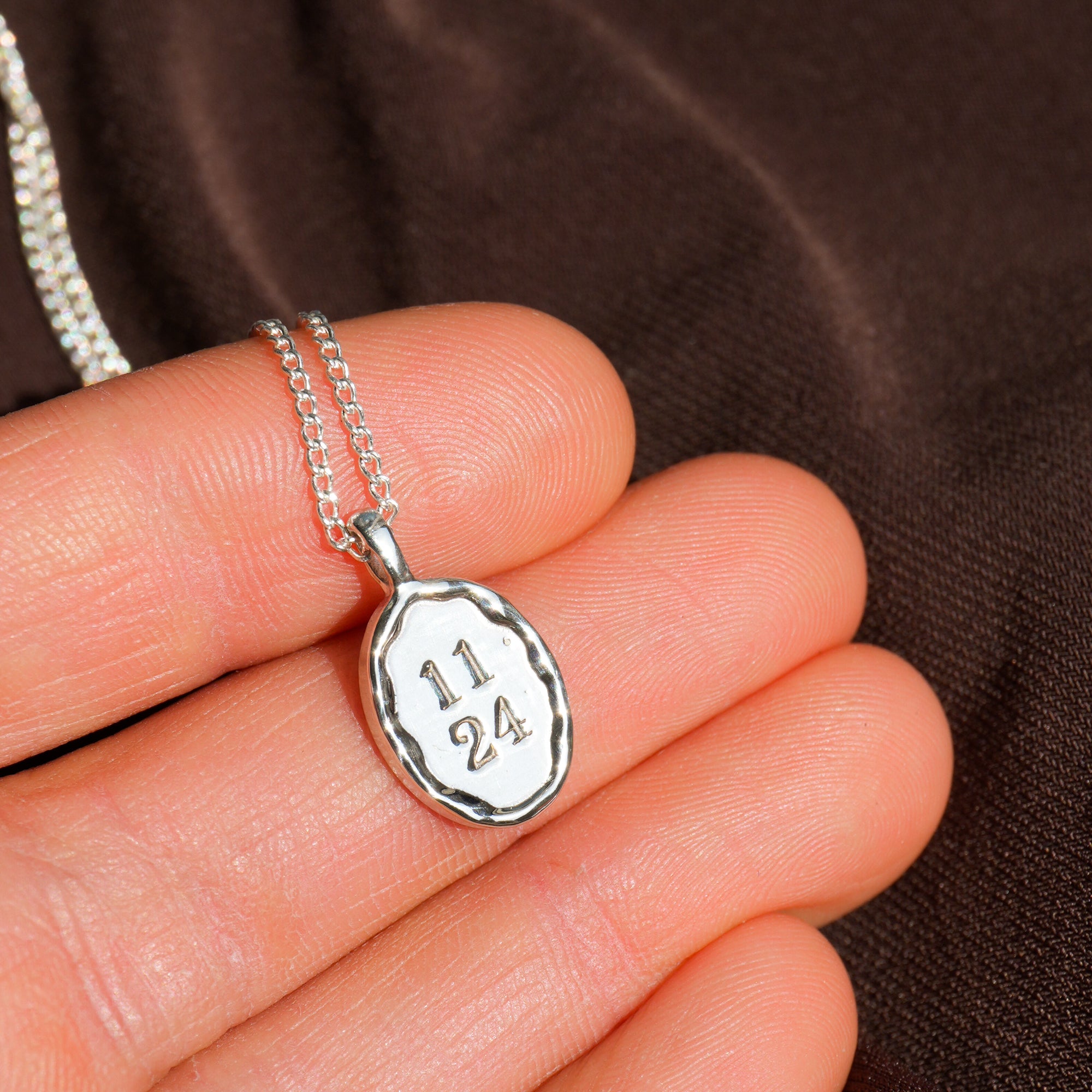 Silver necklace with a pendant engraved with numbers held in a hand against a brown background