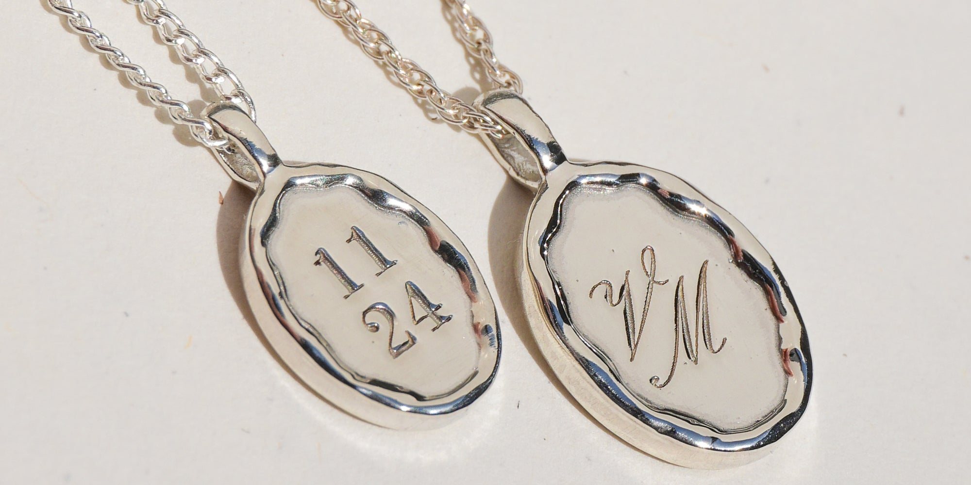 Two silver pendants with engraved text on a light gray background