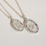 Two silver pendants with engraved text on a light gray background