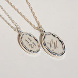 Two silver pendants with engraved text on a light gray background
