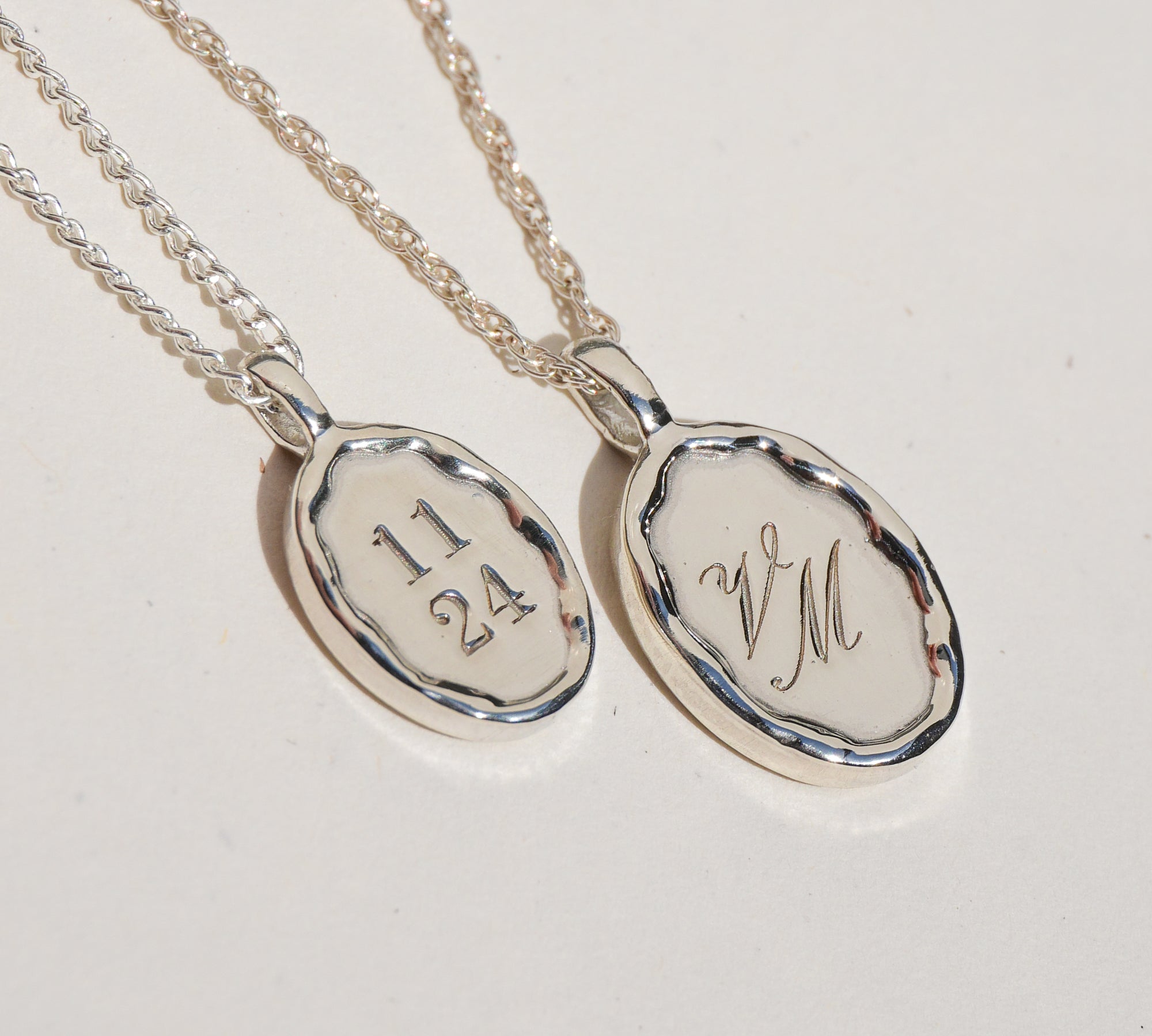 Two silver pendants with engraved text on a light gray background