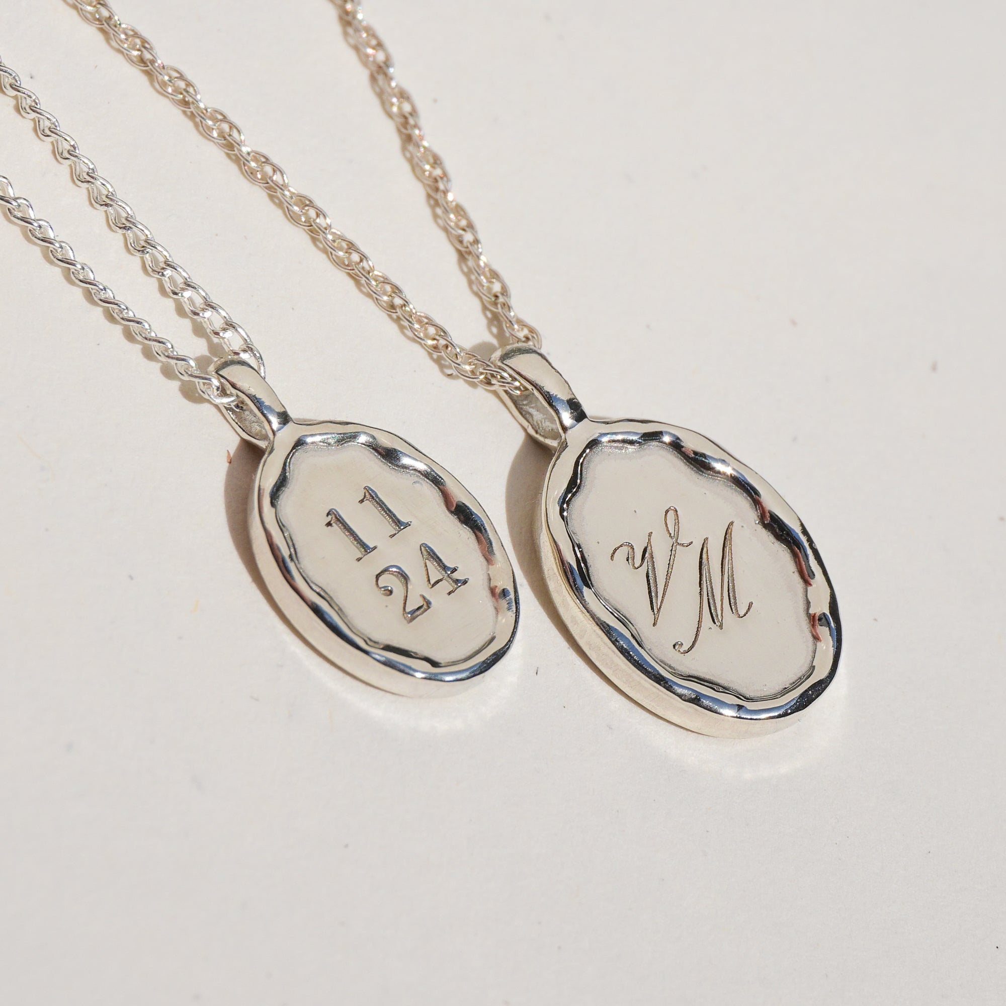 Two silver pendants with engraved text on a light gray background