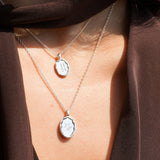 Two silver necklaces with pendants on a person wearing a brown garment.
