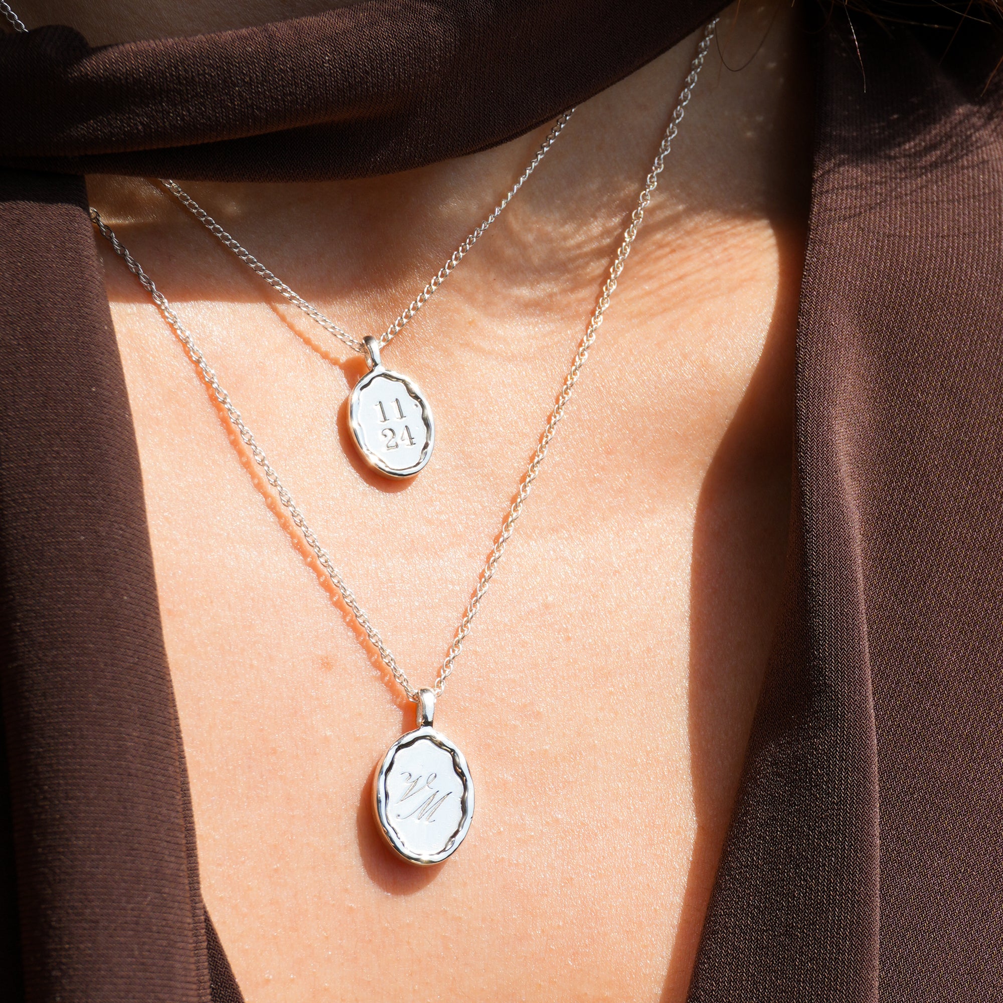 Two silver necklaces with pendants on a person wearing a brown garment.
